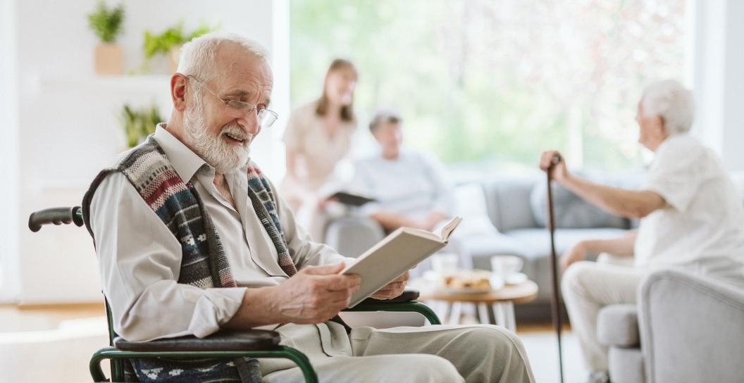 An elderly man sitting in a wheelchair is reading a book
