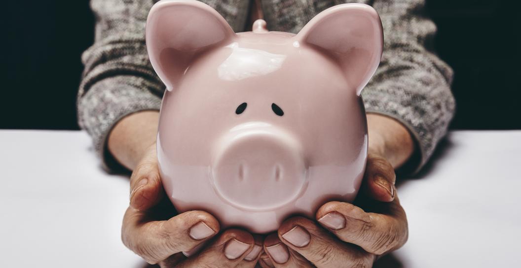 Senior woman holds pink piggy bank.