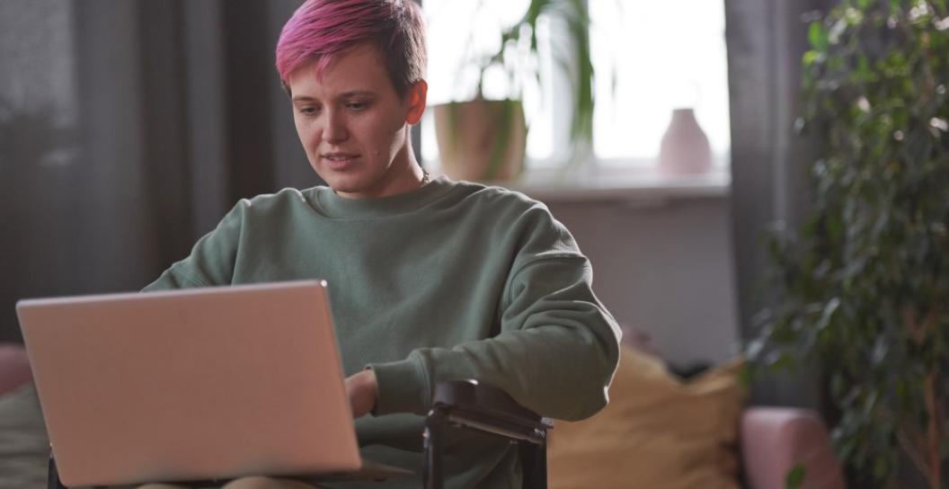 Woman with short, pink hair in wheelchair uses her laptop