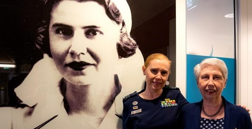 Two women standing in front of large portrait of Second World War nurse