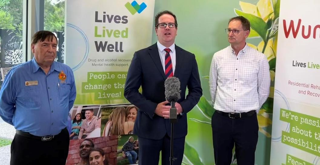 Minister Keogh is in the centre of the image, standing behind a microphone