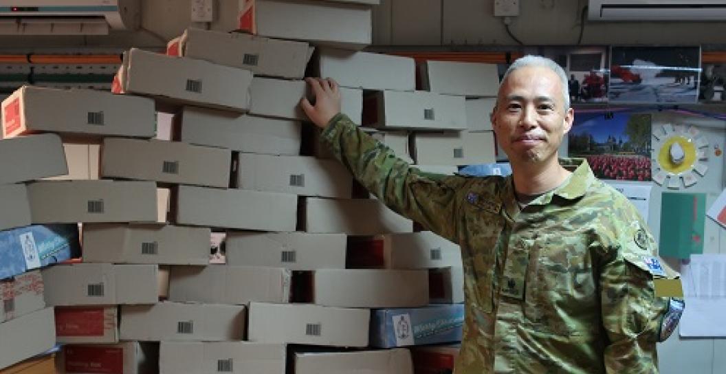 Smiling Army officer poses for camera next to pile of boxes