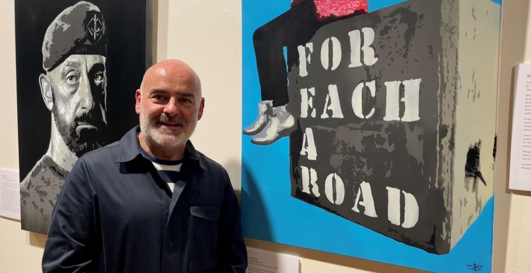 Man posing next to painting saying 'For Each a road'