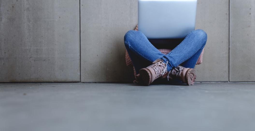 An unidentified person sits on the floor using their laptop