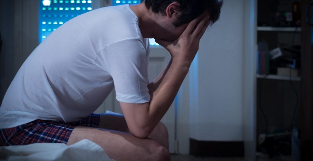 Stock photo of young man sitting on bed with head in hands