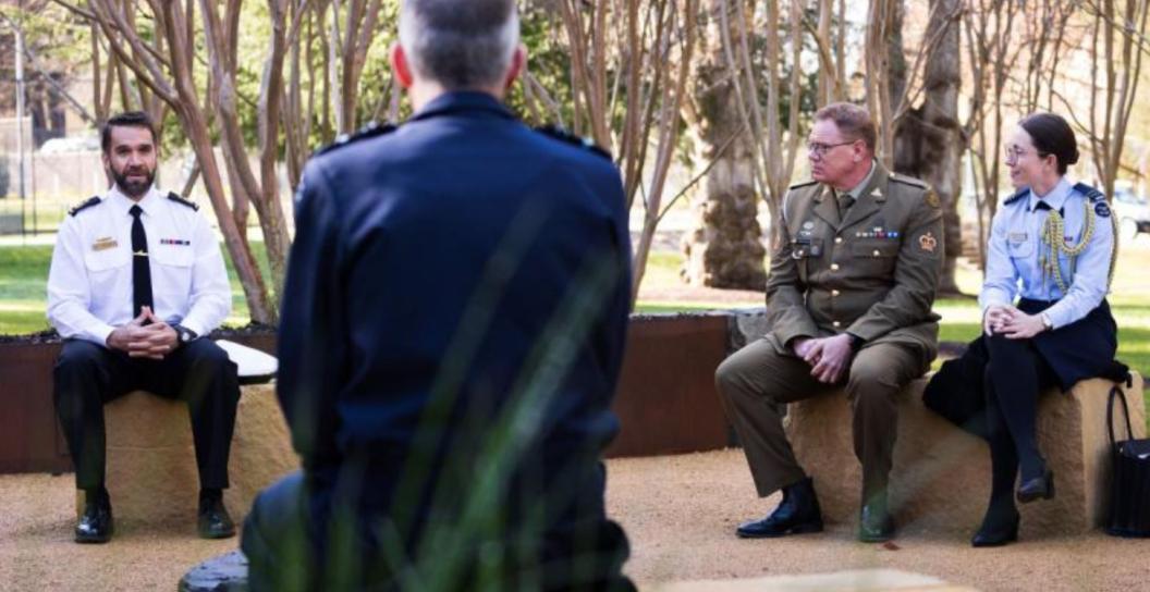 RAAF, Navy and Army personnel chat on seats in open air