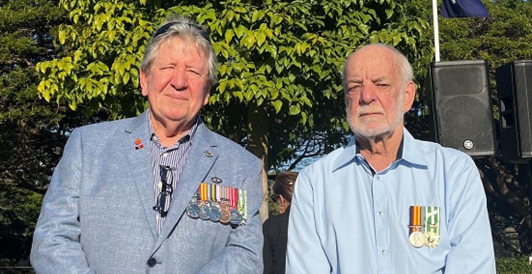 Two older men posing for camera in park. Both are wearing medals.