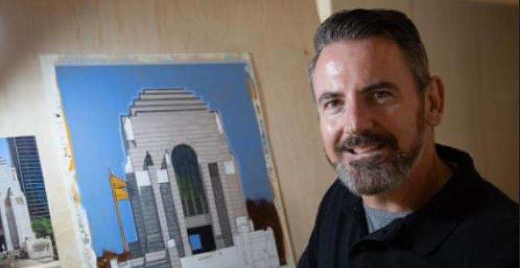 Middle aged man smiling next to painting of Anzac Memorial in Sydney