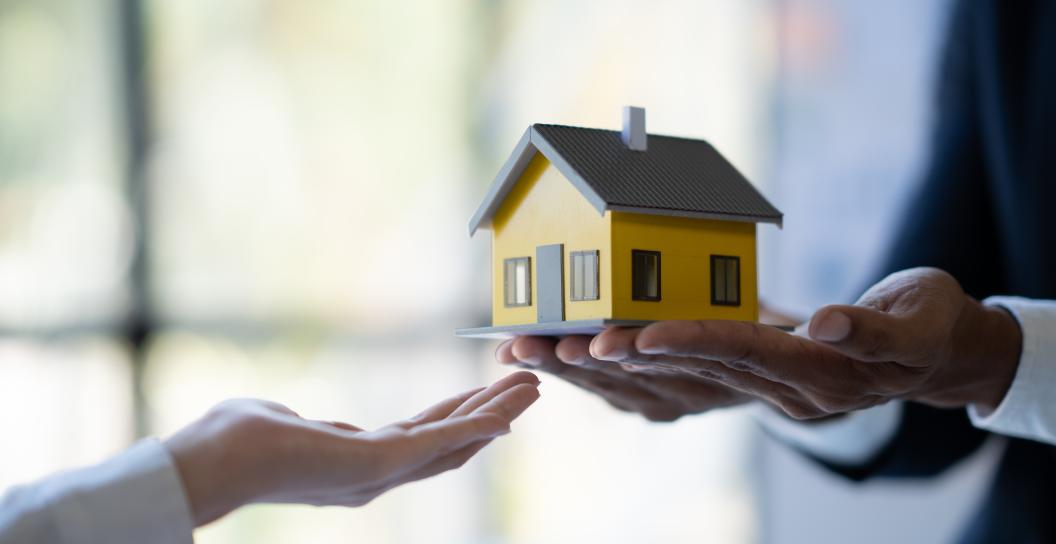 Model of a yellow and grey house, held in palm of hand.