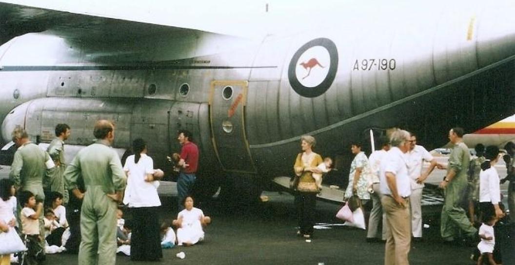 RAAF personnel and civilians stand beside small children on tarmac next to Hercules aircraft
