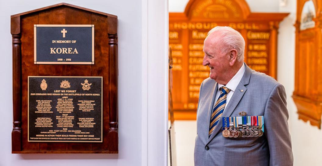 A photo of a older veteran in a suit with medals looking at a Korean War memorial