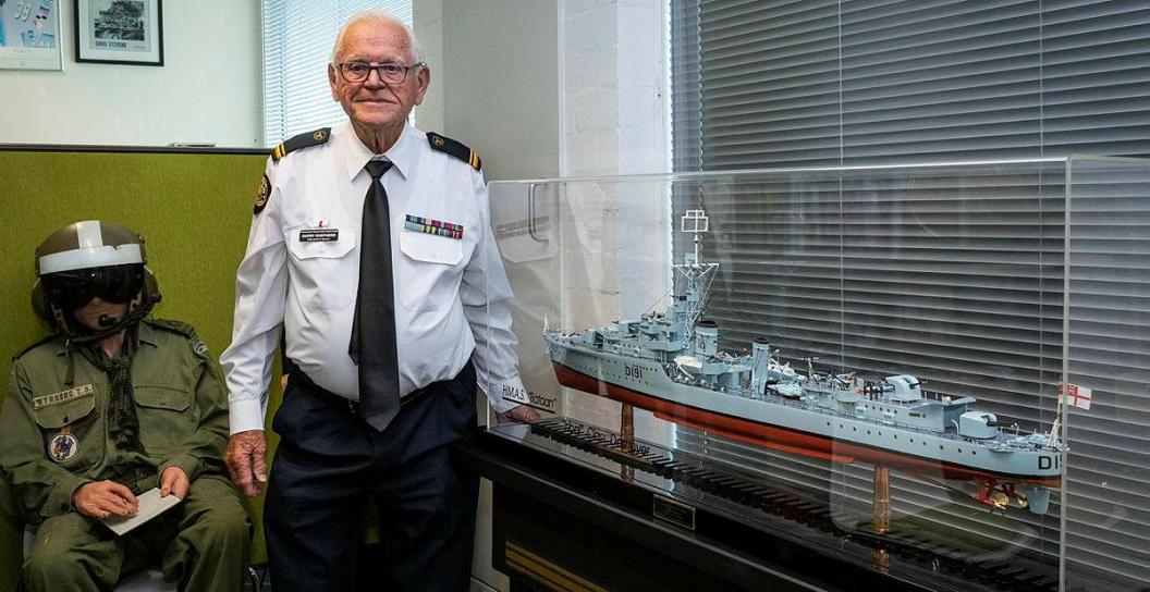 Elderly man in Navy uniform standing next to model of destroyer