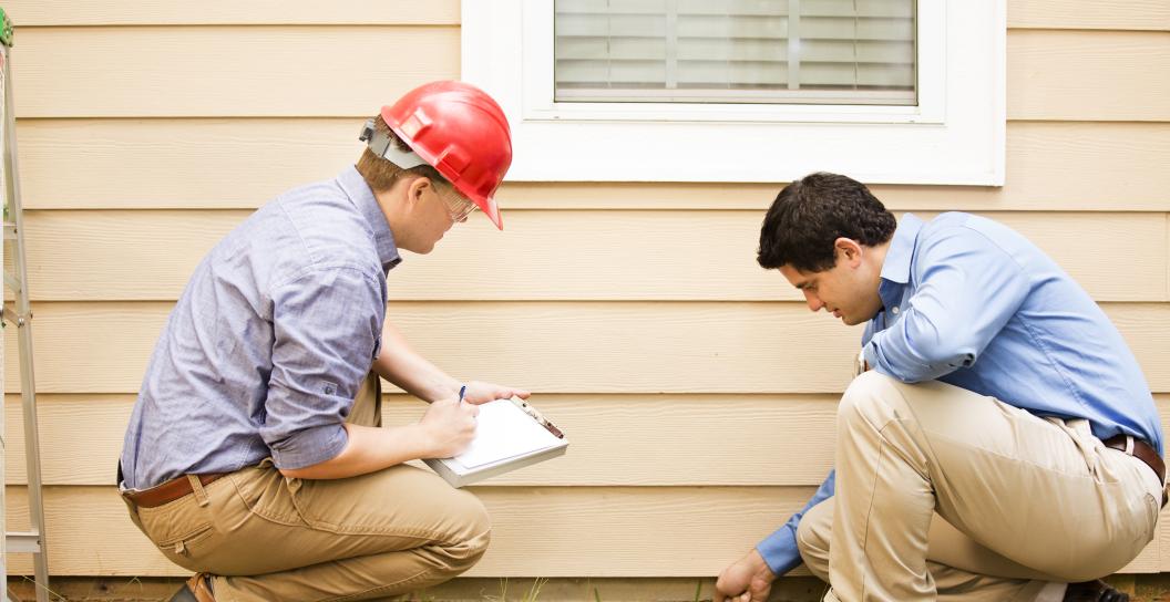 Two crouching men inspecting the side of a house.