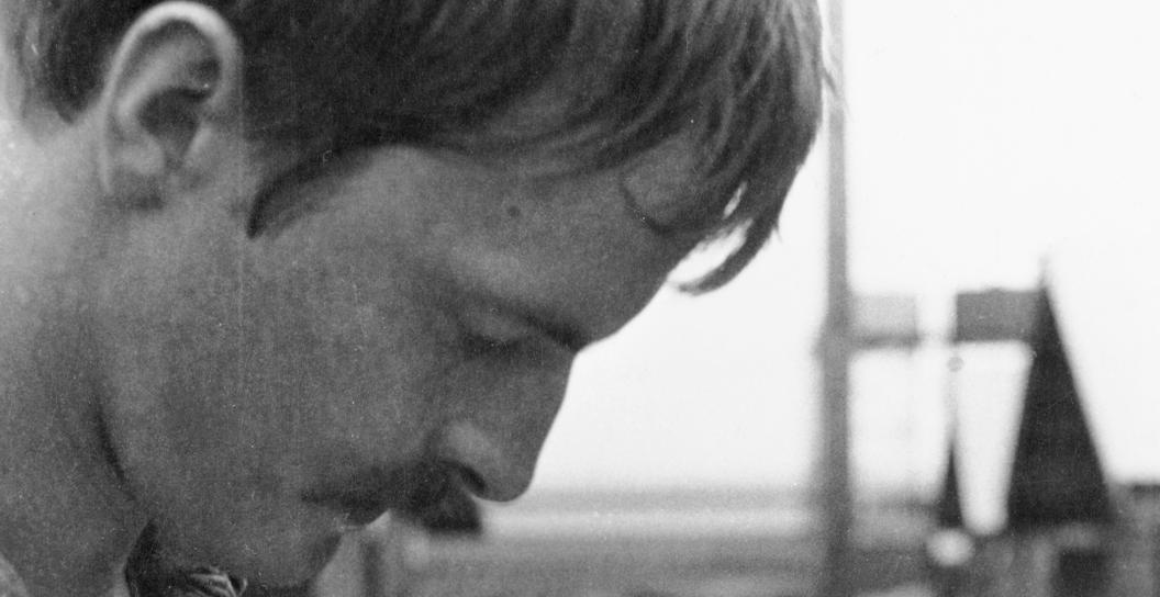 Cropped photo of a young man in battle fatigues looking at a book with bullet holes through it.