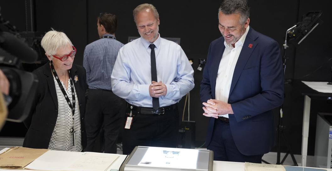 Three people look at documents on a scanner