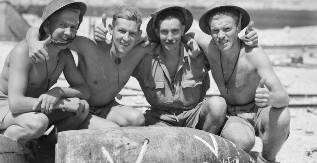 Four smiling soldiers posing with shell
