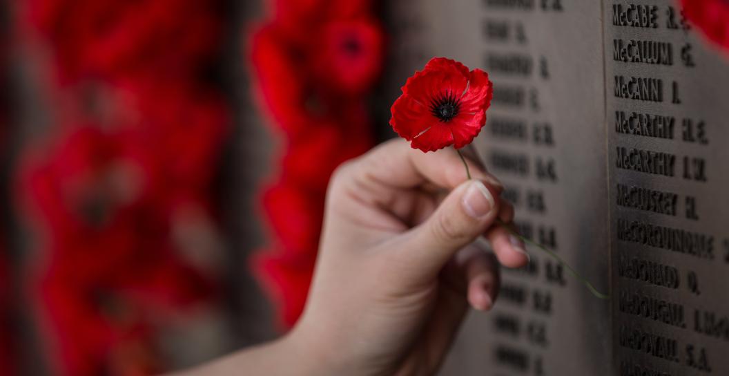 Hand placing poppy on Roll of Honour at AWM