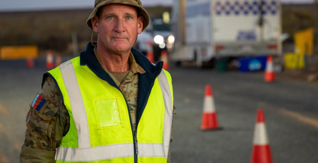 Soldier standing by road with police truck in background
