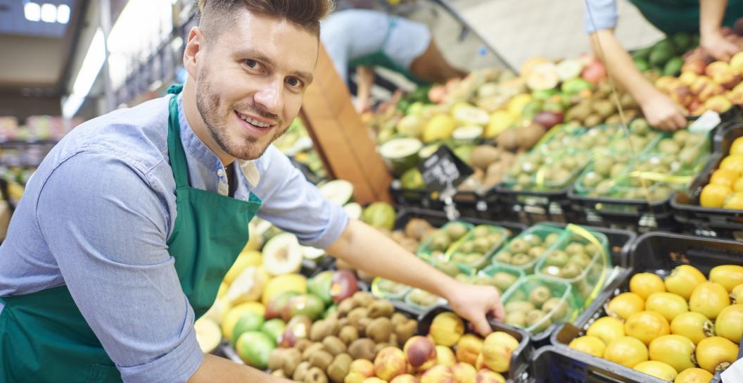 A grocer in a supermarket moving a box of fruit