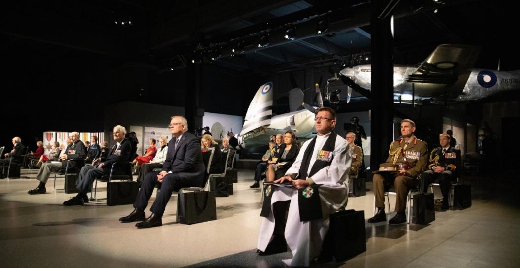 Seated dignitaries widely spaced inside large exhibition hall