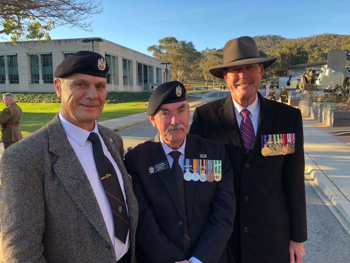 Middle-aged man posing with two older men at Australian War Memorial.